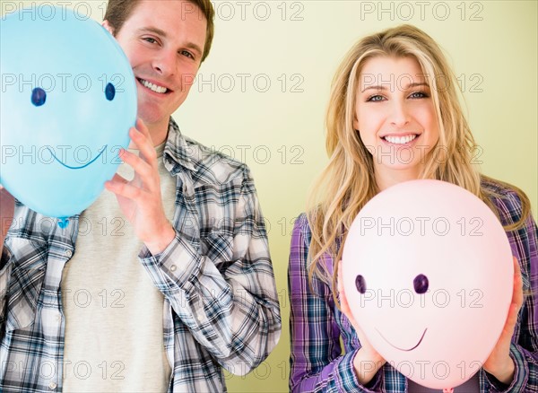 Studio shot of couple holding balloons with smiley faces