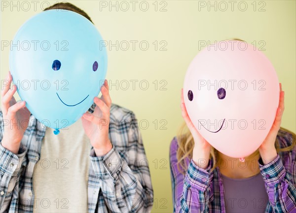 Studio shot of couple holding balloons with smiley faces in front of their heads