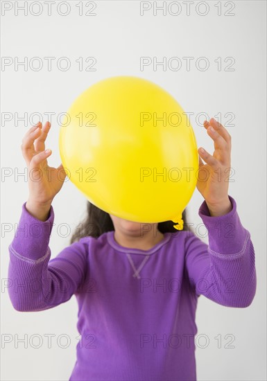 Studio shot of girl (8-9) hiding behind balloon