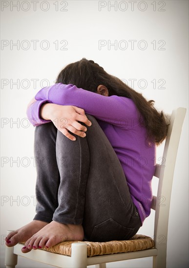 Studio shot of sad girl (8-9) curling on chair