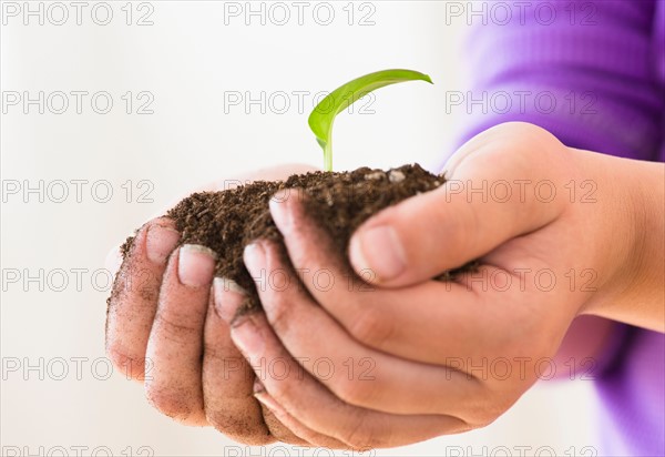 Girl (8-9) holding handful of soil with freshly grown plant