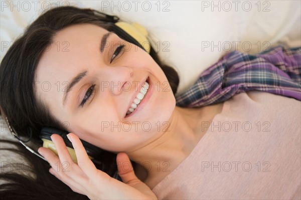 Portrait of young woman lying down on bed and listening to music