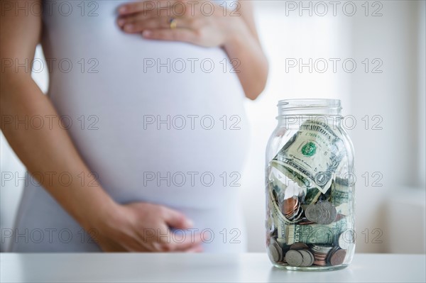Mid section of pregnant woman, jar with money in front