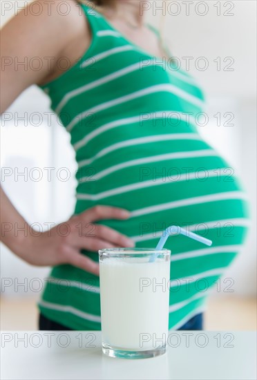 Mid section of pregnant woman, glass of milk in front