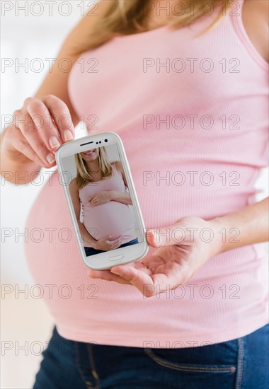 Mid section of pregnant woman holding mobile phone