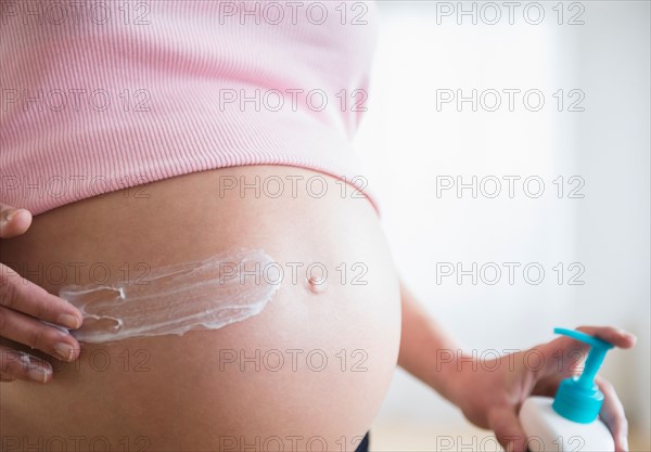 Mid section of pregnant woman applying moisturizer on her belly