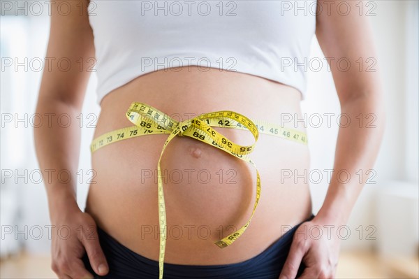 Mid section of pregnant woman with tape measure tied up on her belly