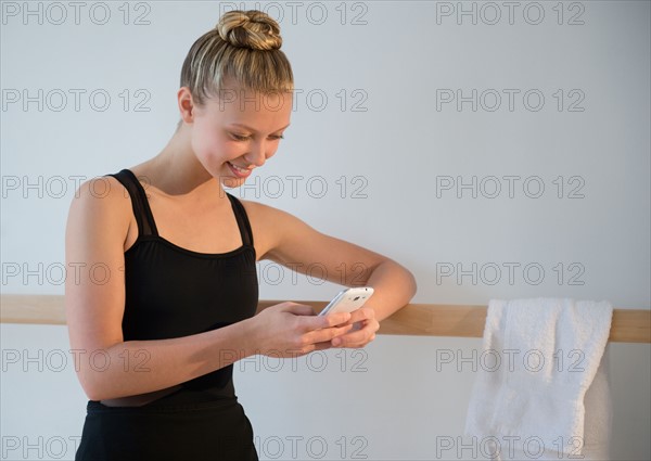 Portrait of teenage (16-17) ballet dancer standing at barre and using mobile phone