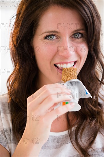 Portrait of young woman eating granola bar