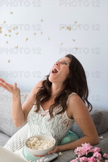 Young woman on sofa, throwing and catching popcorn