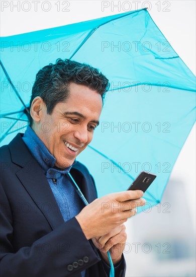 Portrait of man holding blue umbrella and using mobile phone