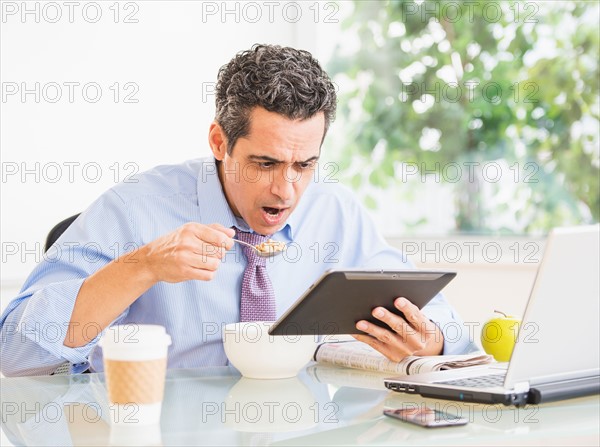 Portrait of man eating and using digital tablet