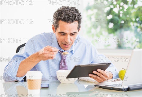 Portrait of man eating and using digital tablet