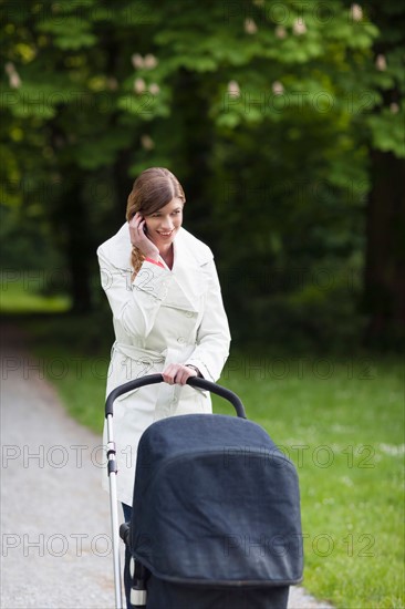 Mother with pram in park talking on mobile phone