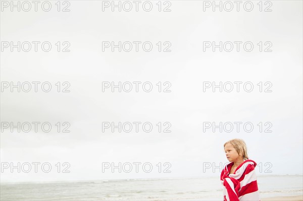 Boy (6-7) wrapped in towel on beach