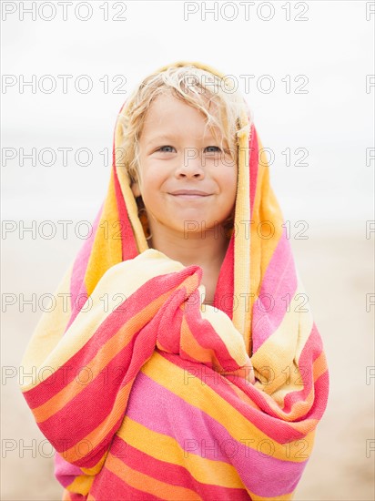 Boy (6-7) wrapped in towel on beach