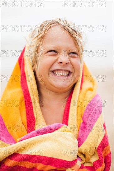 Boy (6-7) wrapped in towel on beach