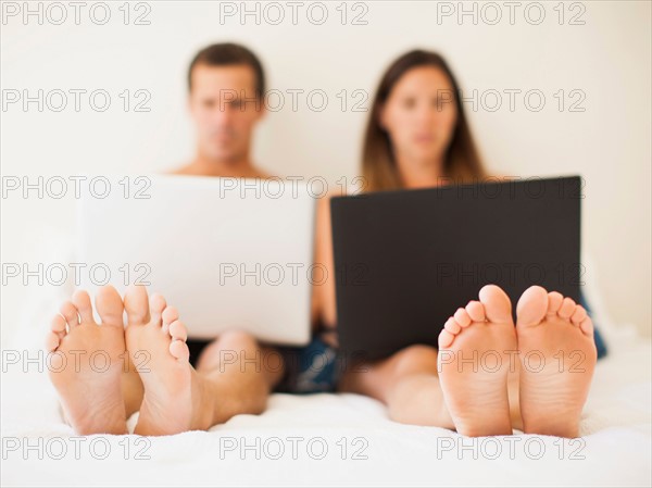 Couple lying on bed with laptops