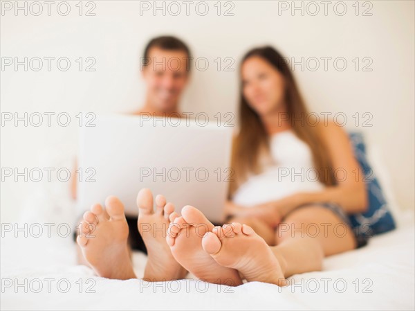 Couple lying on bed with laptop