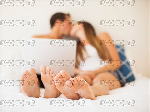 Couple lying on bed with laptop