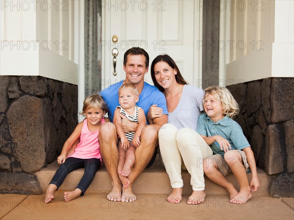 Family with three kids (6-7, 2-3, 6-11 months) sitting in front of house