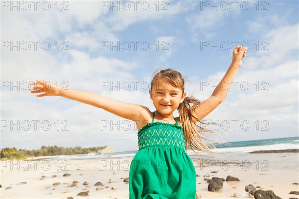 Portrait of girl (6-7) standing on beach with arms raised