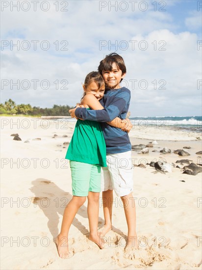 Portrait of girl (6-7) and boy (10-11) embracing on beach