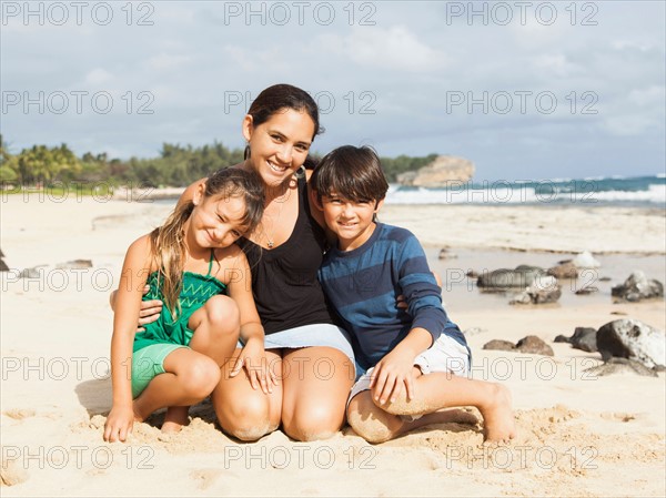 Portrait of girl (6-7) and boy (10-11) sitting on beach with mother