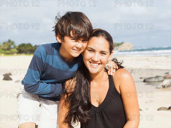 Portrait of boy (10-11) sitting on beach with mother