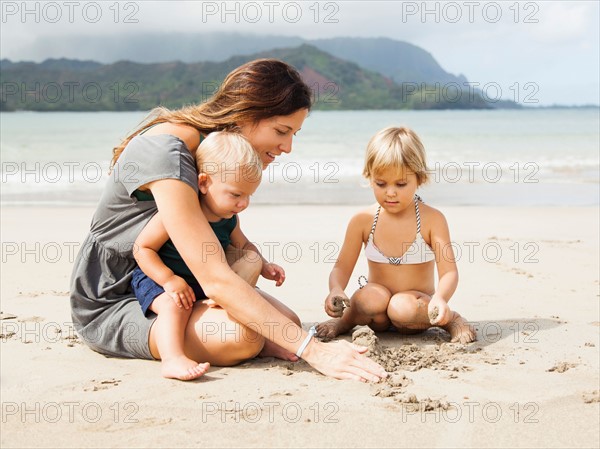 Mother playing with daughters (6-11 months, 2-3) on beach