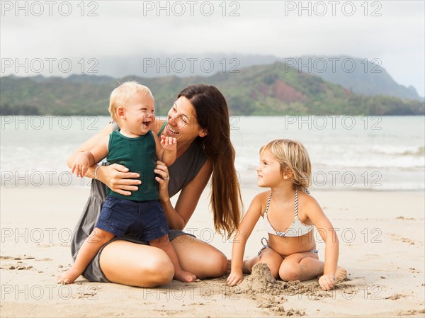 Mother playing with daughters (6-11 months, 2-3) on beach