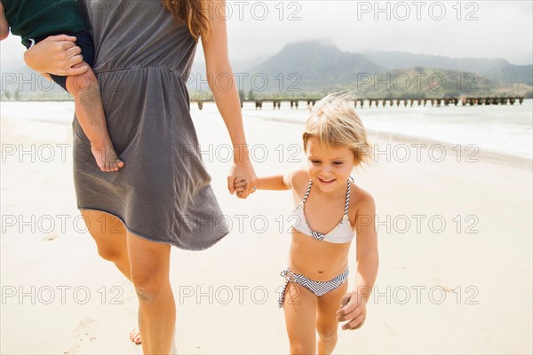 Mother walking with daughters (6-11 months, 2-3) on beach