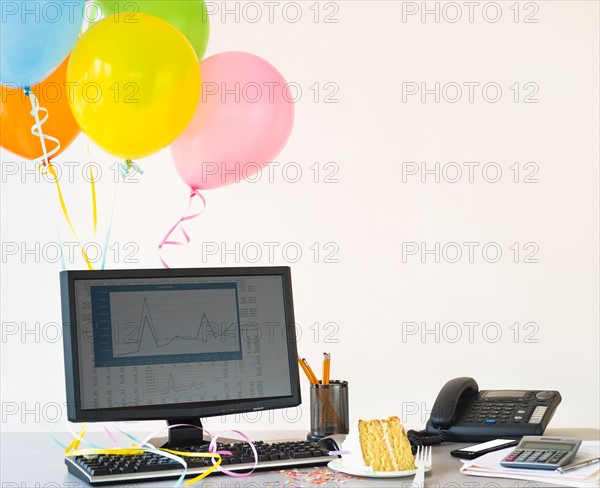 Studio shot of office workspace with cake and balloons.