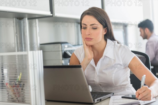 Woman working in office, man in background.