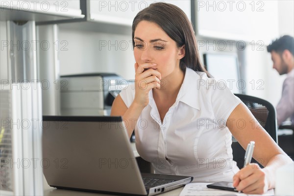 Woman working in office, man in background.