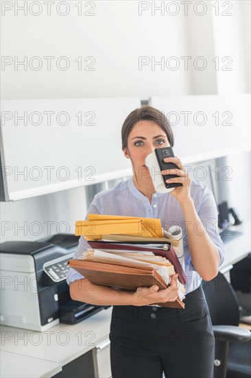 Business woman holding stack of documents and drinking coffee.