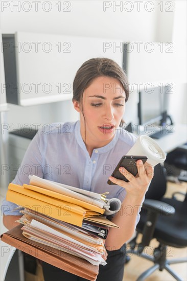 Business woman holding stack of documents and text messaging.