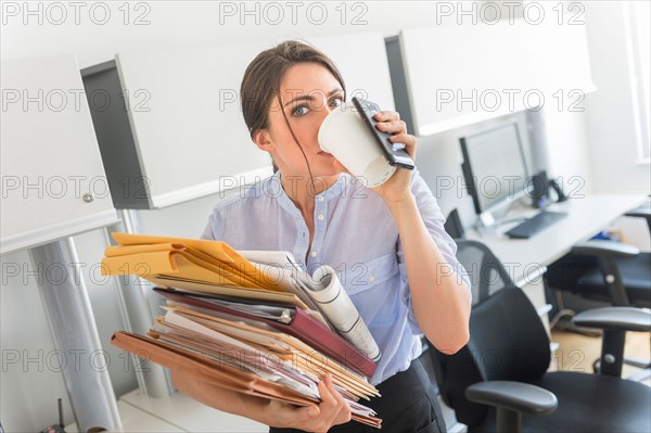 Business woman holding stack of documents and drinking coffee.