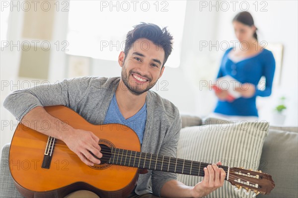 Man playing guitar, woman in background.