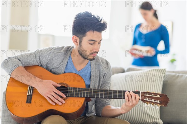 Man playing guitar, woman in background.