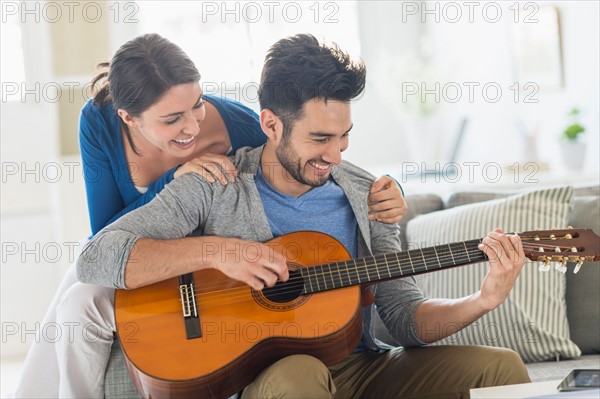 Man playing guitar while woman embracing him.