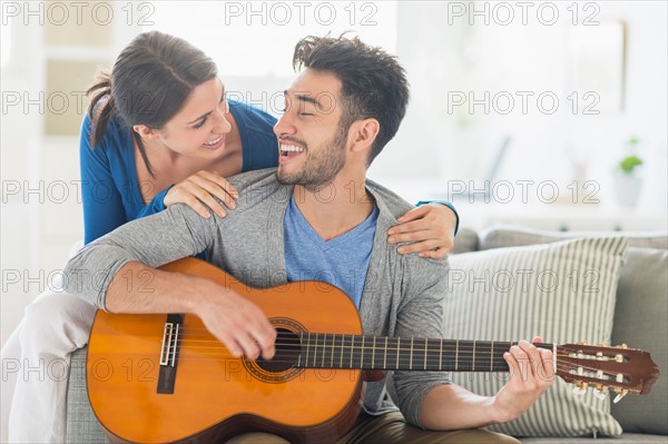 Man playing guitar while woman embracing him.