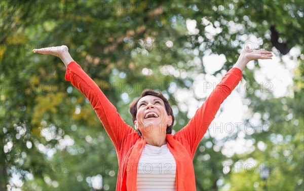 Happy mature woman raising hands in park.