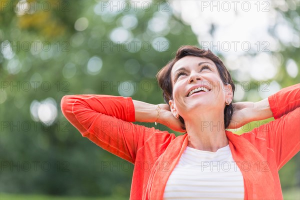 Happy mature woman raising hands in park.