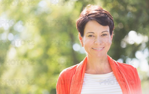 Happy mature woman raising hands in park.