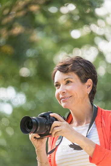 Mature woman holding camera in park.