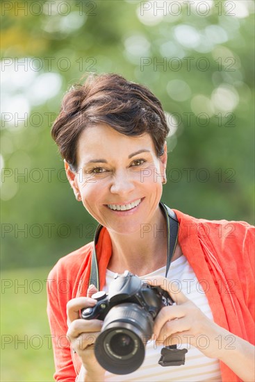 Mature woman holding camera in park.