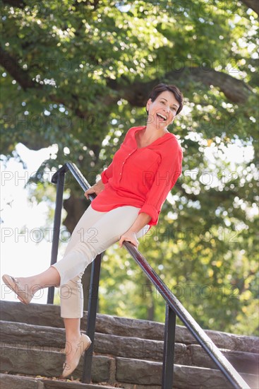 Mature woman sliding down railing in park.