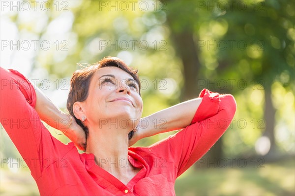 Happy mature woman raising hands in park.