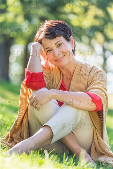 Mature woman sitting on grass in park.